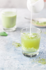 Iced Matcha green latte in glasses with matcha powder on light background.