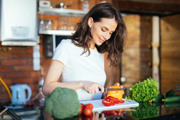 Happy young housewife cutting fresh peppers in kitchen