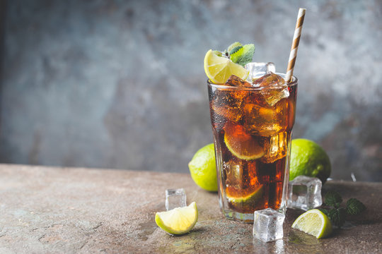 Fresh made Cuba Libre with brown rum, cola, mint and lemon on gray stone background