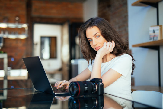 Concentrated young woman watching tutorial online on modern laptop device using wireless internet connection. Pensive professional female photographer working remotely at digital netbook