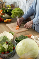 Close-up of man's hand cutting carrot on chopping board with knife on wooden kitchen counter