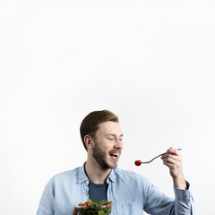 Young man eating red cherry tomato and salad in white background