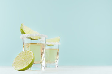 Alcohol cocktail - tequila with salty rim, piece lime in shot glasses in modern elegant pastel blue...
