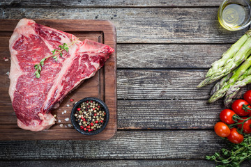 Raw T-bone Steak with fresh herbs and oil on dark wooden background, top view