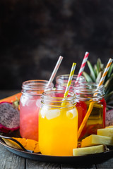 Glasses of tasty fresh tropical juices with fresh tropical fruits, Papaya Pine Apple Mango Dragon on dark background.