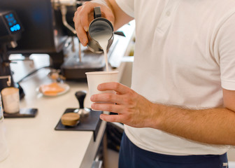 Young barista pouring and serving  to go paper cup of coffee