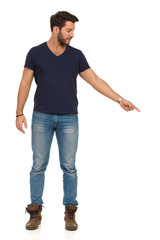 Handsome Man In Jeans T-Shirt And Boots Is Pointing Down And Looking Away