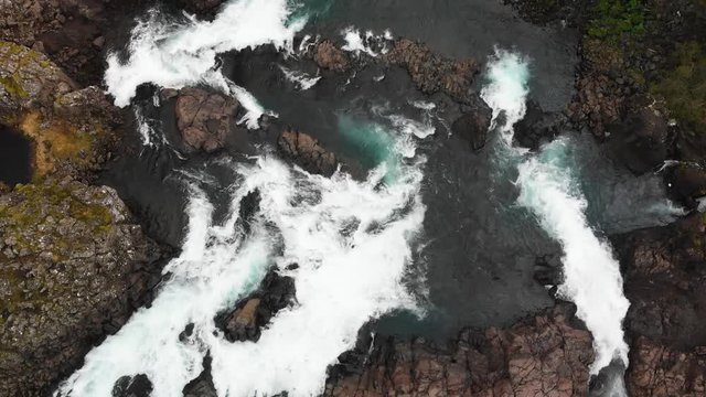 Flying straight over the gorgeous waterfall Glanni in Iceland seeing the turquoise water whirling around in the river, surrounded by a rocky landscape and some greenery