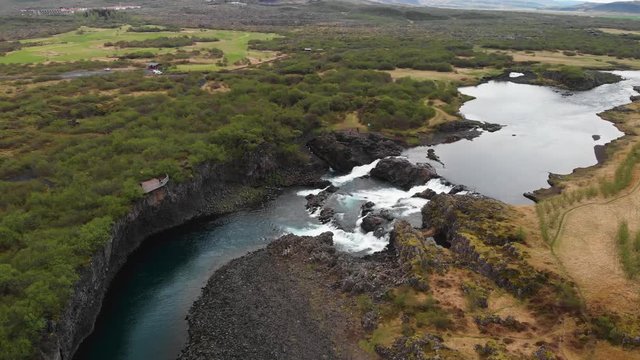 The less crowded but beautiful waterfall Glanni seen from above, surrounded by a magical Icelandic landscape with lush green bushes and majestic mountains in the background