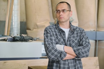 Portrait of male worker in industrial production. Confident man in glasses gloves in casual shirt with crossed arms.