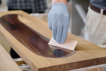 Closeup of workers hand covering wooden plank with finishing protective cover for wood
