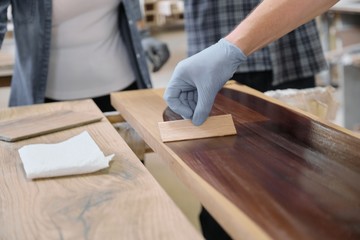 Closeup of workers hand covering wooden plank with finishing protective cover for wood