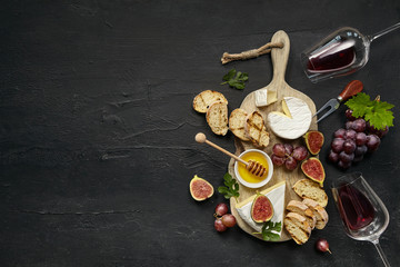 Two glasses of red wine and a tasty cheese plate with fruit, grape and toasted bread on a wooden...
