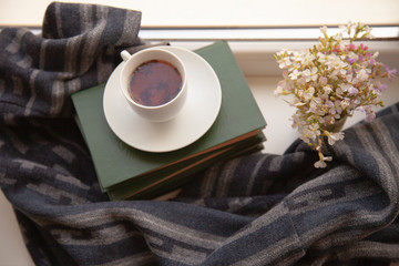 white cup with tea on the books on the windowsill with a scarf