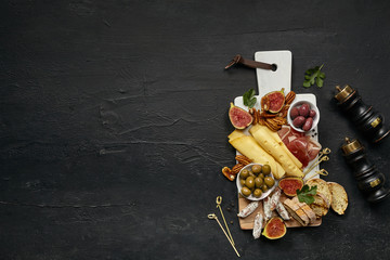 Fototapeta na wymiar Top view of tasty cheese plate with fruit, grape, nuts, olives and toasted bread on a wooden kitchen plate on the black stone background, top view, copy space. Gourmet food and drink.
