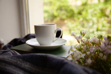 white cup with tea on the books on the windowsill with a scarf