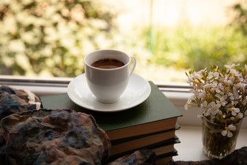 white cup with tea on the books on the windowsill with a scarf