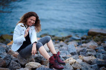 fashionable girl dressed in white jacket and wide trousers posing near sea in the evening