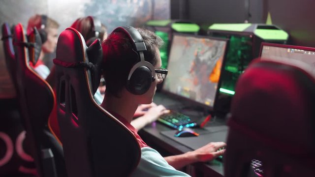 Young gamer plays a video game, side view, uses gaming mouse and keyboard, illuminated coral color and multicolor neon, cybersportsman.