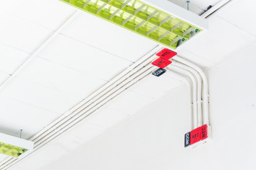 White electric PVC pipe in red and black are connected to power lines or electrical wires, Ethernet UTP cables, internet and light boxes on building wall. Concept for construction and system building.