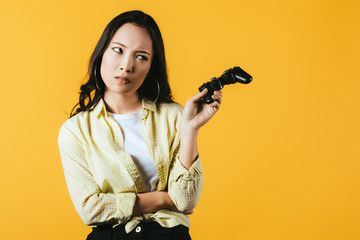 KYIV, UKRAINE - APRIL 16, 2019: attractive asian girl holding joystick, isolated on yellow