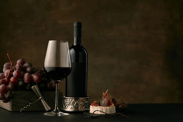 Front view of tasty fruit plate of grapes with the wine bottle, cheese and wineglass on dark studio background, copy space to insert your text or image. Gourmet food and drink.