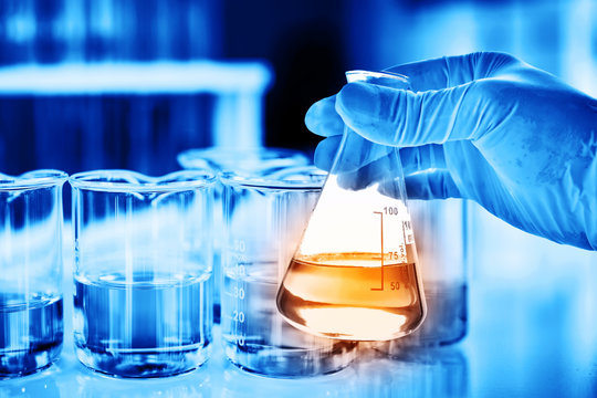 Flask in scientist hand with lab glassware background in laboratory. Science or chemical research and development concept. 