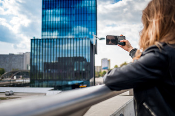 Young smiling woman taking photo by smartphone on the modern city street