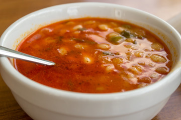 White beans in tomato sauce in a bowl with a spoon in on wooden table at a restaurant.