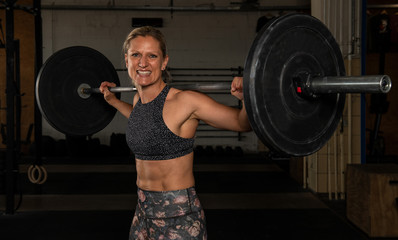 Eine durchtrainierte Frau mittleren Alters macht die Übung Clean und Jerk. Fitnesstraining mit der Langhantel. Training mit Gewichten.