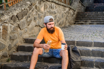 Urban lifestyle and unhealthy nutrition. Carefree hipster eat junk food while sit on stairs. Hungry...