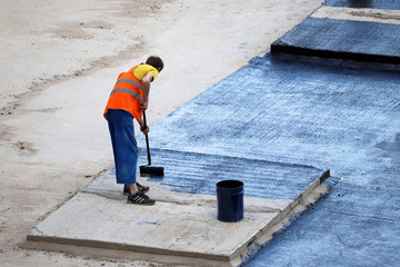 Worker in overalls fills the roof of underground parking with bitumen. Works for waterproofing on a construction site