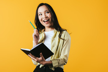 smiling asian girl with notebook and pen, isolated on yellow