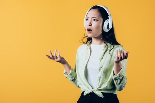 Frustrated Asian Girl Listening Music With Headphones, Isolated On Yellow