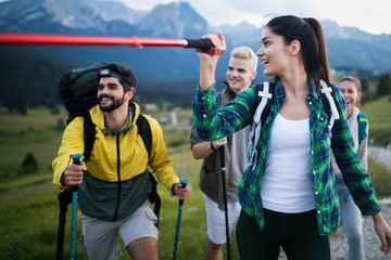 Group of hikers with backpacks and sticks walking on mountain. Friends making an excursion