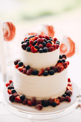 Beautiful cake covered with icing cream, summer berries on the top. Style and food photography