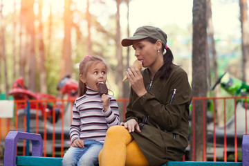 Fototapeta premium Mother and daughter sitting on bench in the park, eating ice cream