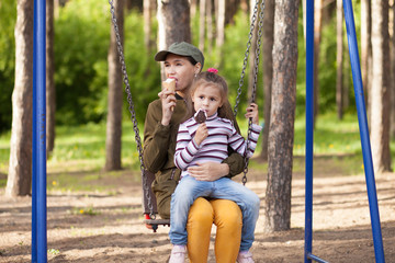 Mother and daughter sitting on teeter-totter, in the park, eating ice cream