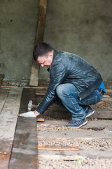 Worker with a hammer in dirty clothes hammering a nail into a wooden floor