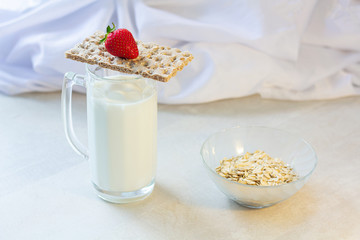 milk in a glass for beer. dry dietary bread, red strawberry, oatmeal on a white wooden kitchen table, morning, breakfast fitness and food cooking. white background, healthy lifestyle