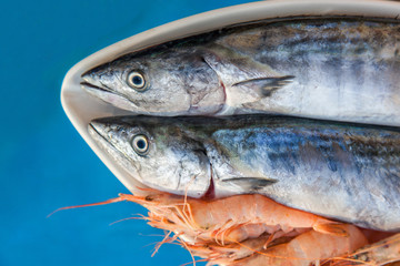 Two fresh silver sardines and pink shrimps are on plate in front of pool ready to be grilled on sunset healthy foot diet dinner