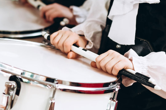 A closeup of the hands of a drummer at a parade. Children's ensemble in white shirts. White new snare drum, white sticks. The concept of a military parade and march.