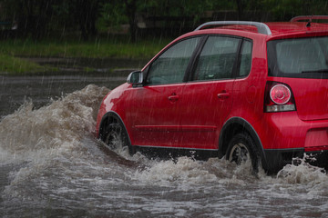 Red car rides in heavy rain on a flooded road
