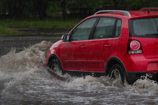 Red Car Rides In Heavy Rain On A Flooded Road