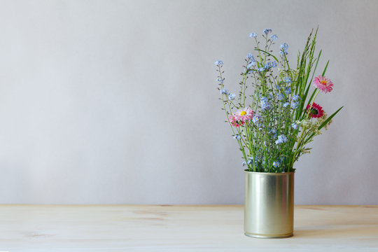 still life fresh tender fragile beautiful wildflowers and green grass in metal can on wooden table on gray background, copy space