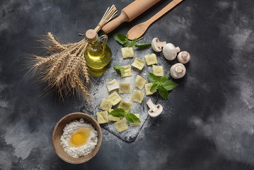 Fototapeta na wymiar Italian raw ravioli with mushrooms, basil, flour, wheat, olive oil on dark background.Shavuot Jewish holiday food concept