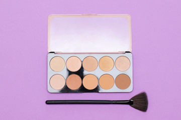 Palette with a tone of beige shades and makeup brush on a purple background