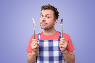 Man in apron holding cutlery fork and knife