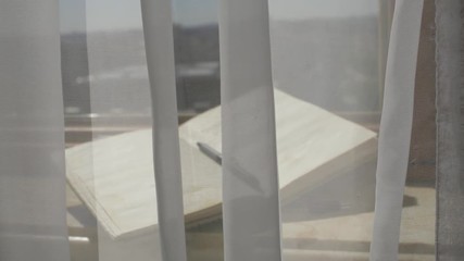 Open agenda with a pen at marble sill of an open window. Blowing grey transparent curtains - Powered by Adobe