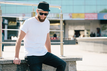 Hipster handsome male model with beard wearing white blank t-shirt and a baseball cap with space...